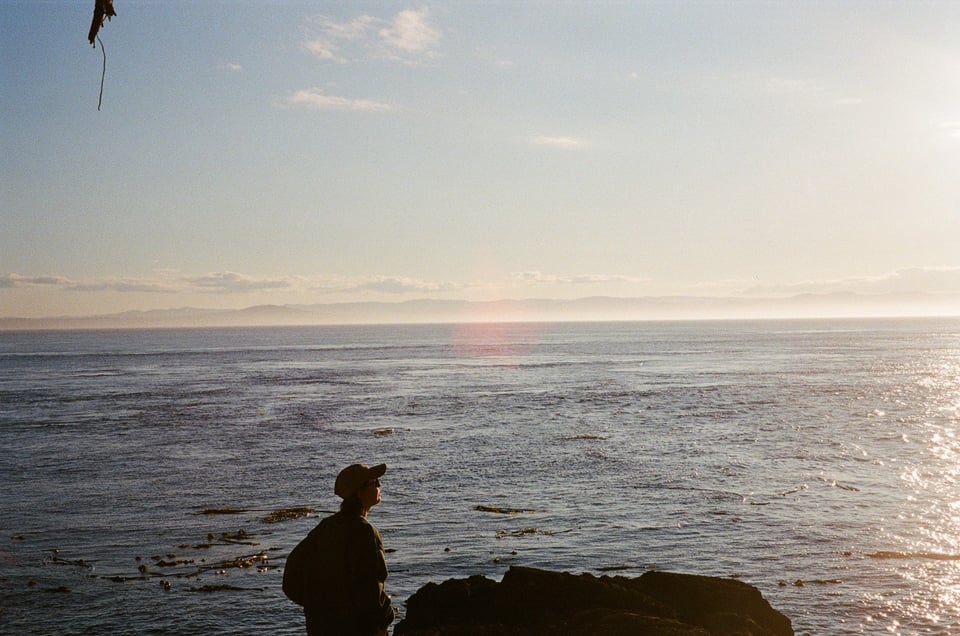 The sea at sunset. A person is silhouetted next to a rock.