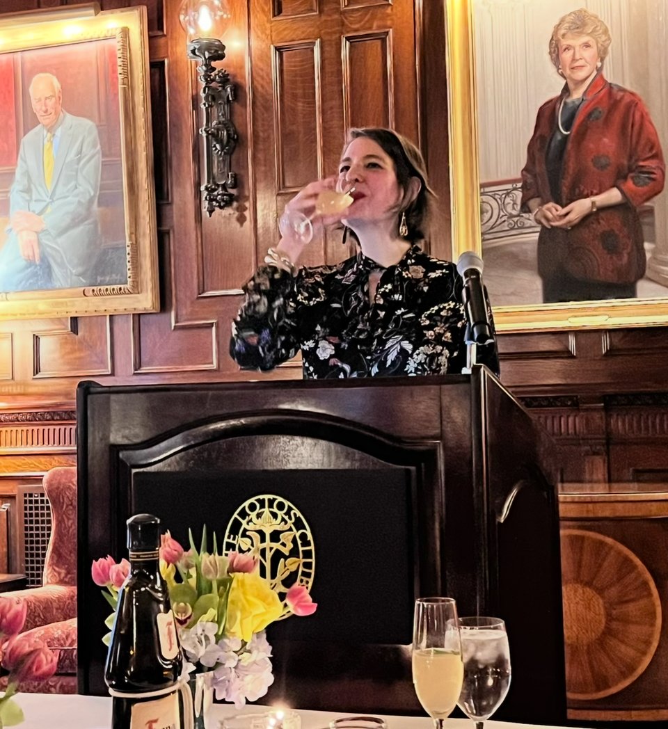 Amanda Schuster sips an Old Cuban cocktail from a flute at the podium at the Lotos Club, NYC on April 16, 2025