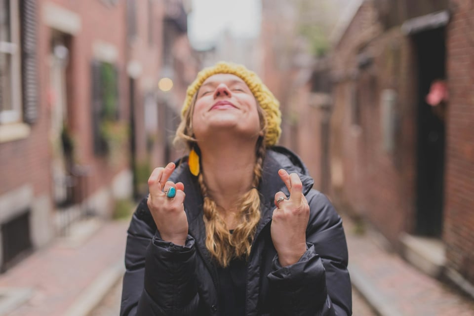 A woman, eyes closed, crossing her fingers and facing the sky (as though she is wishing very hard for something). Photo by Dayne Topkin on Unsplash.