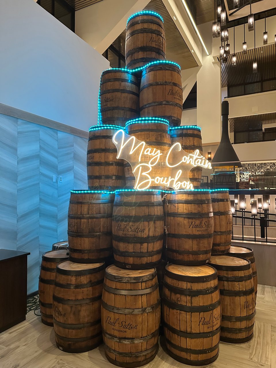 Photo of a stack of barrels wit the electric sign "May Contain Bourbon" in script