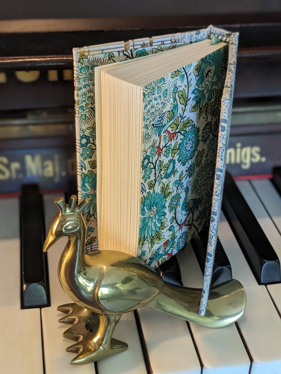 A photograph of an octavo-sized handbound hardcover copy of A Dubious Clamor, propped open to display peacock-themed endpapers.
