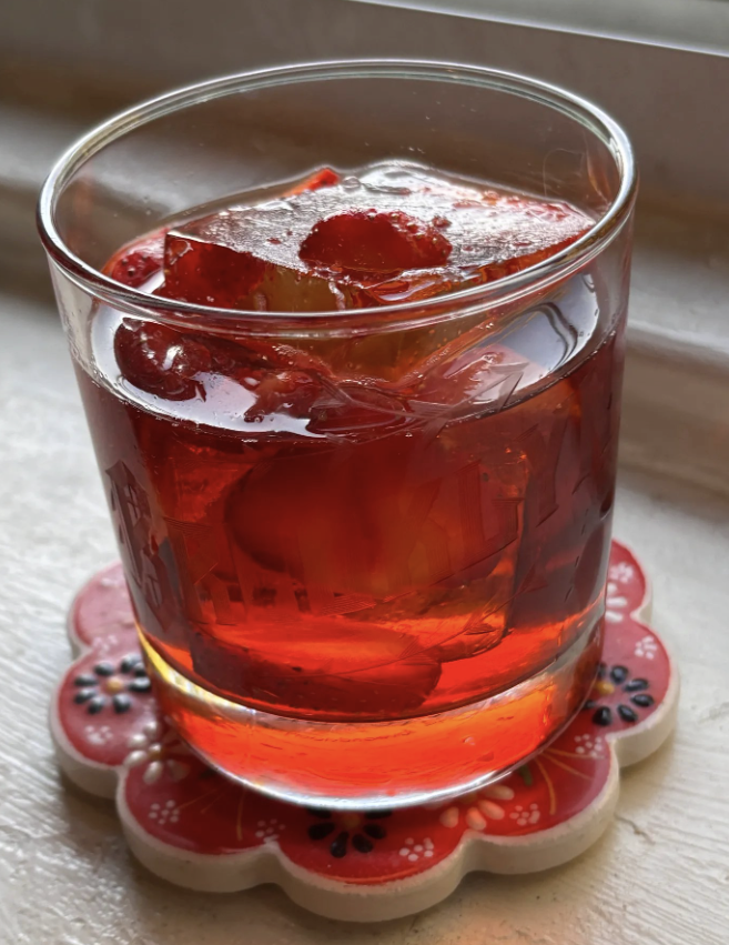 Bright red Negroni cocktail variation made with macerated fresh strawberries, aperitivo liqueur, gin, and rosé sitting on a windowsill in sunlight