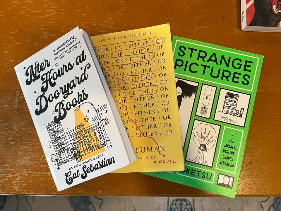 Three paperback books are posed in a fan shape on a wood coffee table.