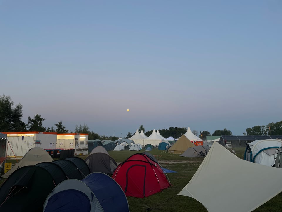 Full moon sets in the early morning dawn over our a campground full of tents.