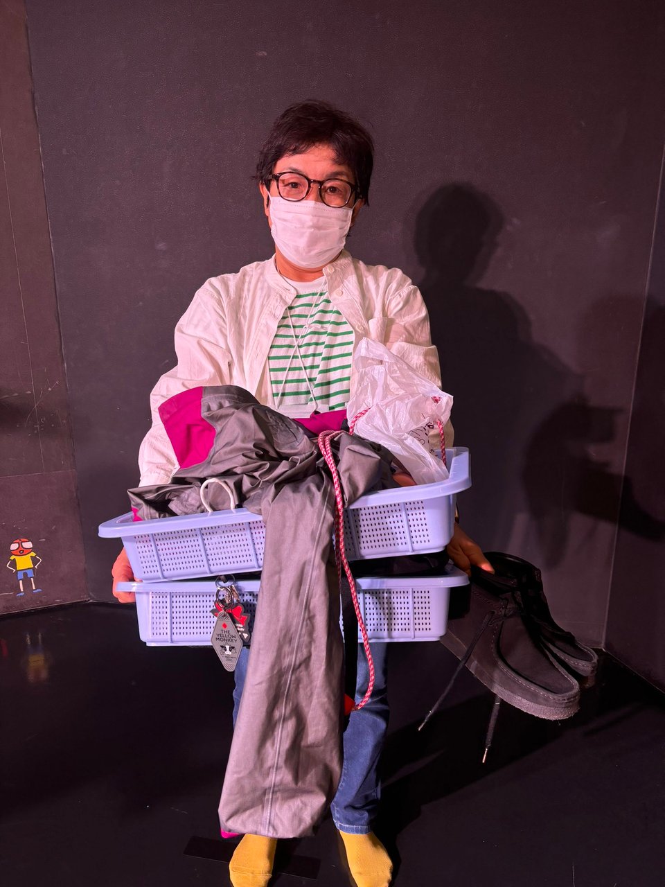 A person holds two airport trays full of jackets and other belongings. Their shoes are off of their feet and in one of their hands
