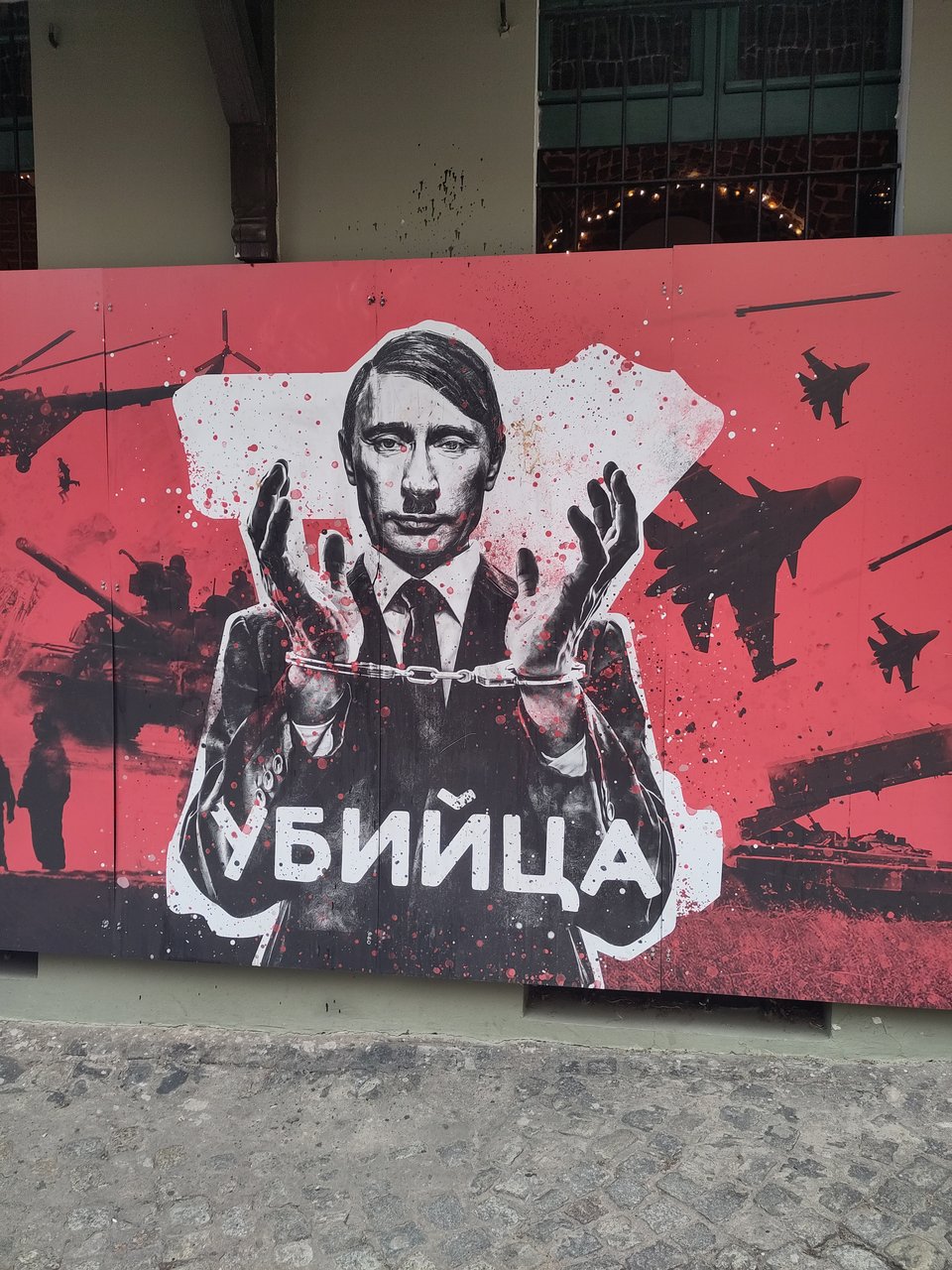 Wandbild auf dem Putin mit Hitler-Optik in Handschellen abgebildet ist.