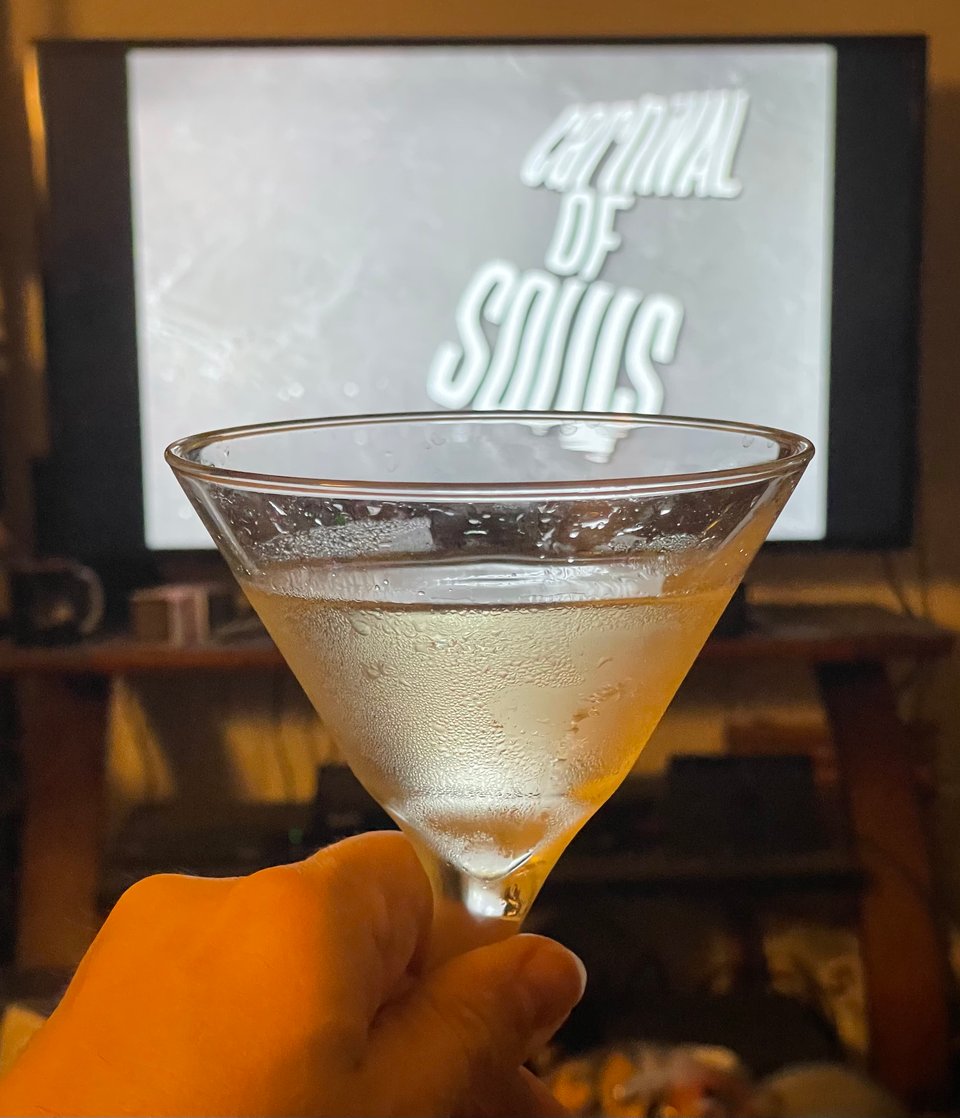 A hand holds a martini up to a TV screen. On the screen is the title text for the film, Carnival of Souls
