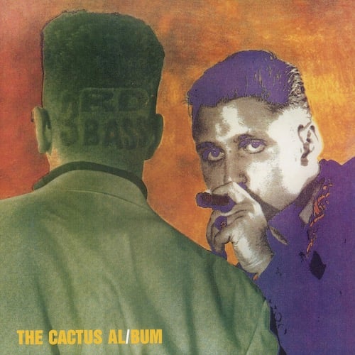 A picture of MC Serch on the left and Prime Minister Pete Nice on the right, both of 3rd Bass. MC Serch has his back to us. He is tinted green and has tall curly hair that has been shaved on the sides. On the back of his head/neck "3rd Bass" has been shaved into his hair. Pete Nice is tinted purple and is facing us. His mouth is obscured by the big cigar he's holding in his mouth. The background is dark orange.