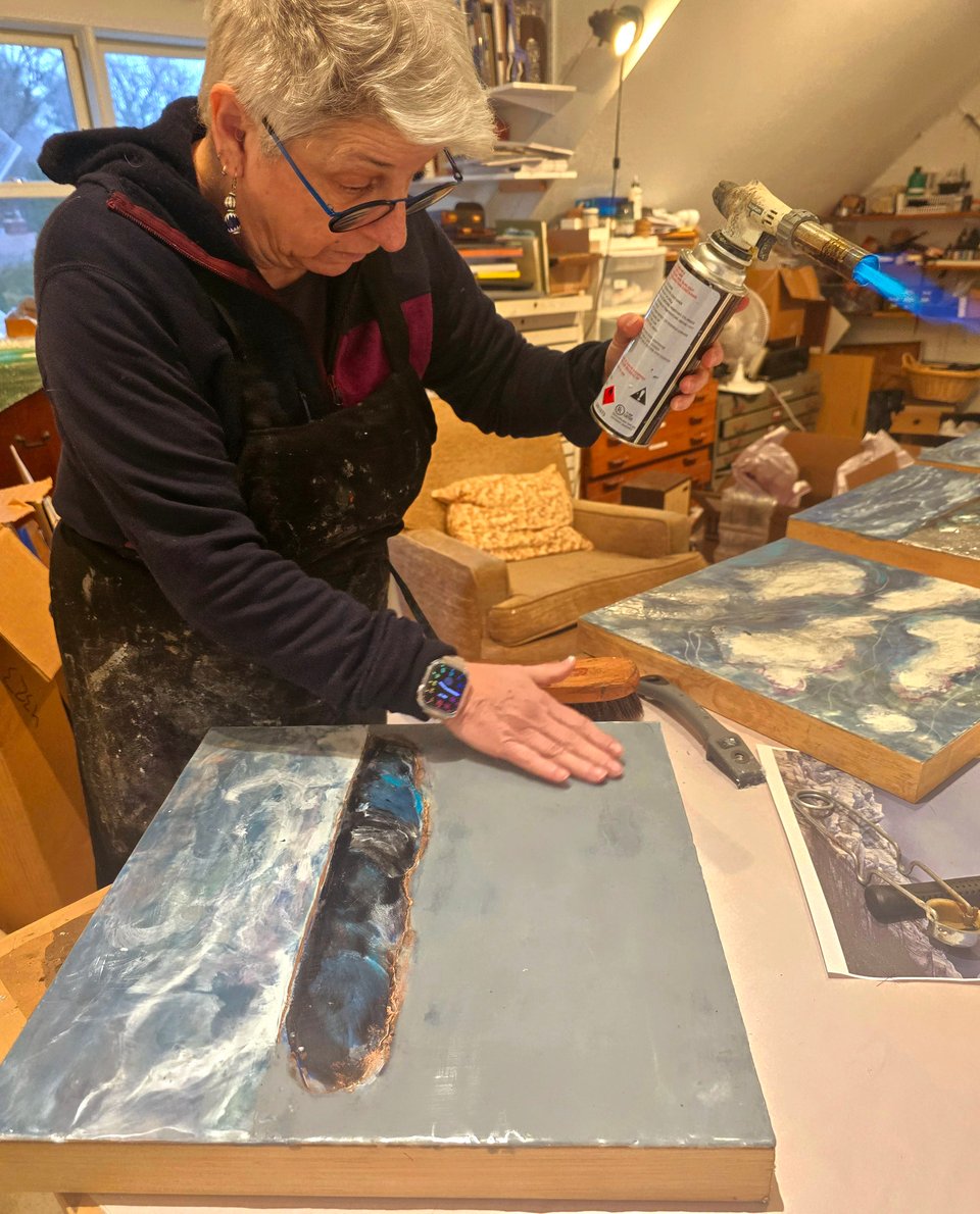 photograph of Leslie working in studio with a torch and some paintings