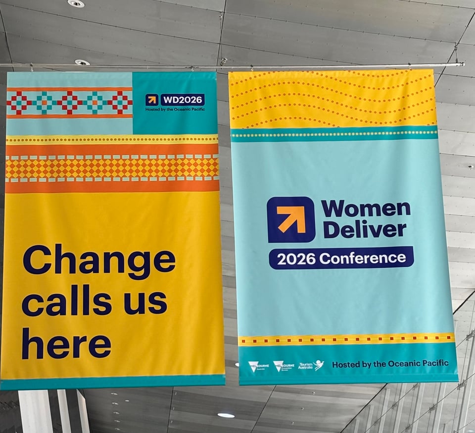 Women Deliver 2026 banners hanging up at the convention centre in Narrm (Melbourne). Banner on the left reads: WD 2026, Change calls us here with a yellow background. Banner on the right reads (on light blue background) Women Deliver, 2026 Conference; Hosted by the Oceanic Pacific.