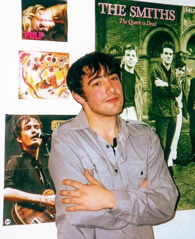 a young ferran leaning on a wall filled with posters