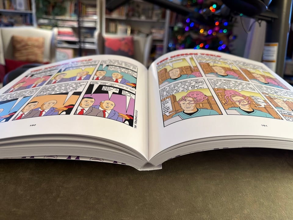 Tom Tomorrow book Our Long National Nightmare open to a spread showing lay-flat binding and two colorful pages with one comic on each. In background, bokeh of chairs, pillows, and Christmas tree.