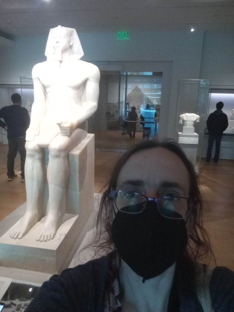 Me, wearing a KN-95 mask, in front of a giant seated statue of Egyptian king Menkaure at the Museum of Fine Arts, Boston.