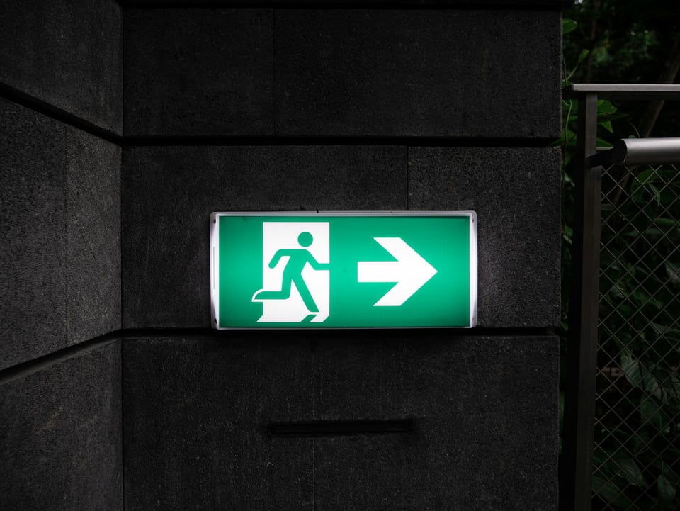 A green "exit" sign on a dark background. Photo by Andrew Teoh on Unsplash.