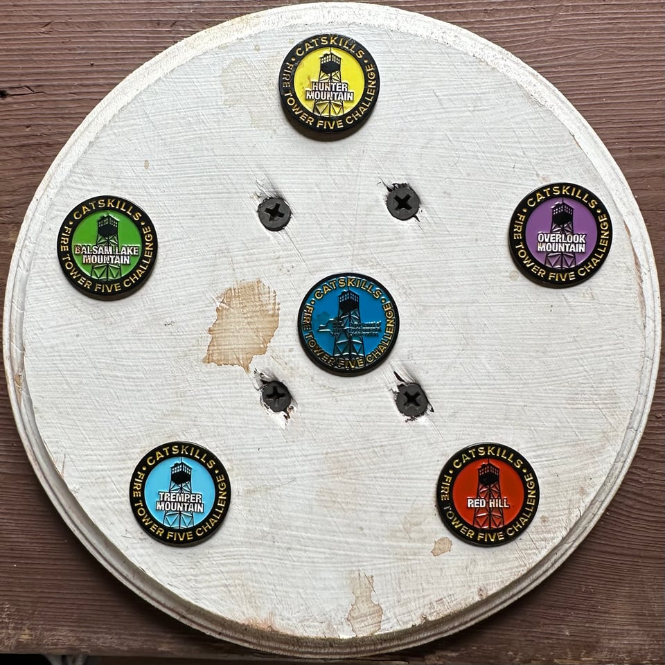 Photo of a white wooden disk with 6 pins placed on it commemorating the Catskills Fire Tower Challenge