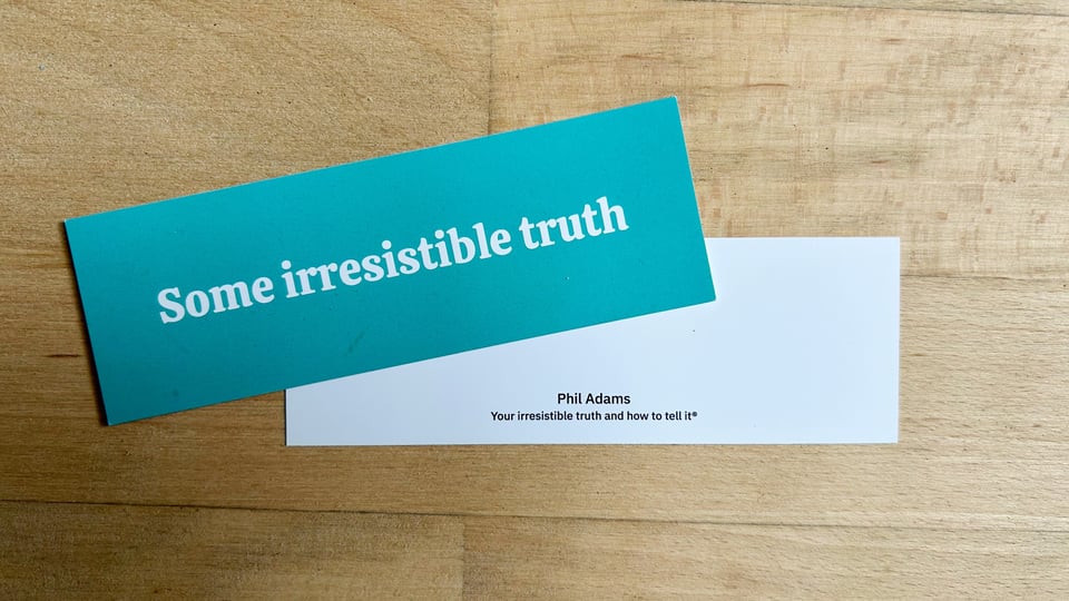 Photograph of two overlapping bookmarks, showing the front and back respectively. The front has a mint green background, with large white text, which says, "Some irresistible truth." The back is mostly blank apart from some small text which says, "Phil Adams. Your irresistible truth and how to tell it®."