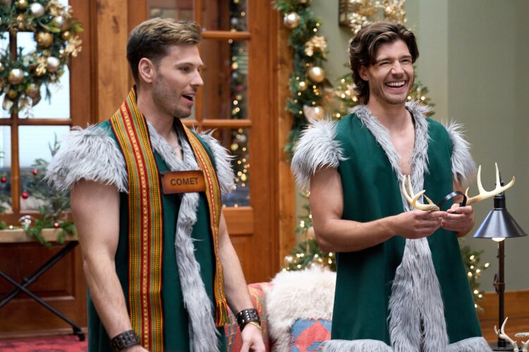 two men dressed as santa claus with green coats, one is holding reindeer antlers and the other is wearing a sign saying "Comet"