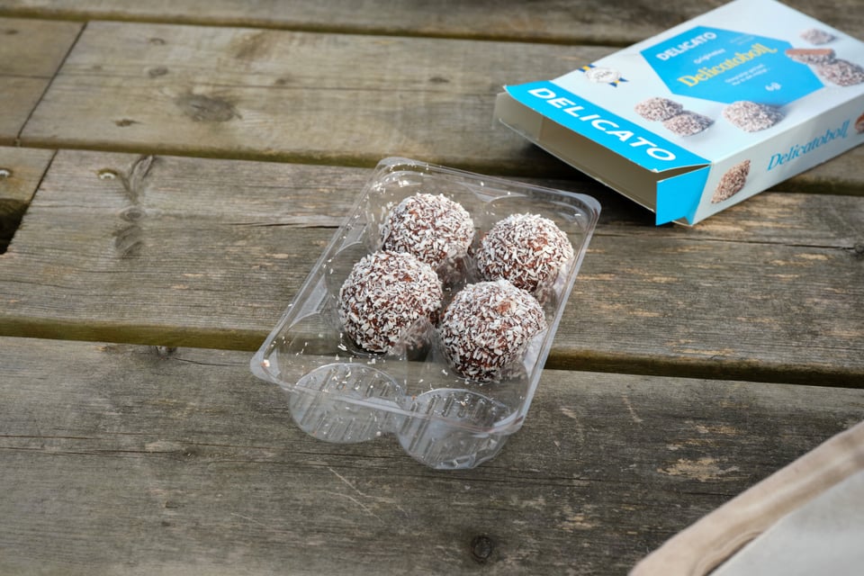 Four brown balls covered with coconut flakes in a plastic tray.