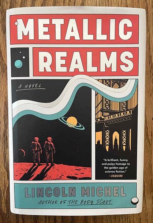 The hardcover novel Metallic Realms by Lincoln Michel. The cover is colorful, with metallic silver letters for the title. The artwork evokes classical science fiction and also New York.