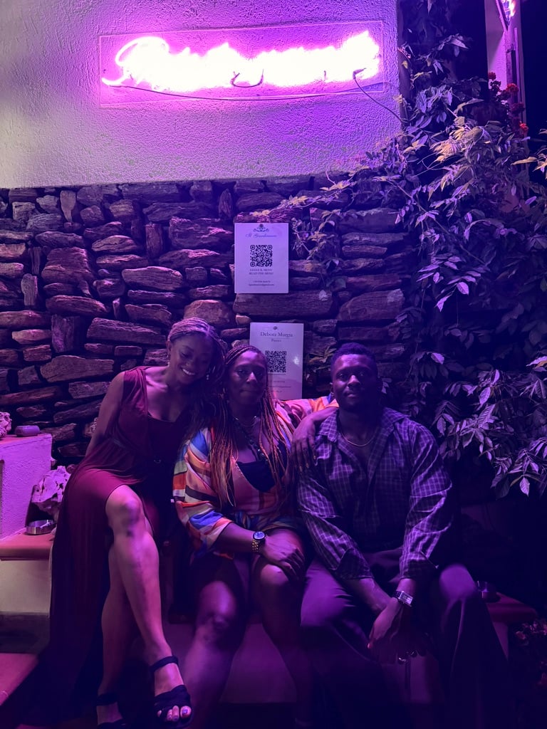 My siblings and I sit together at a venue lit by purple and pink neon lighting, with a rustic stone wall and greenery behind us.