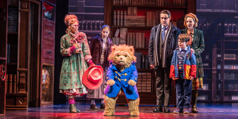 Paddington, a bear in a blue coat, gives the audience a hard stare.