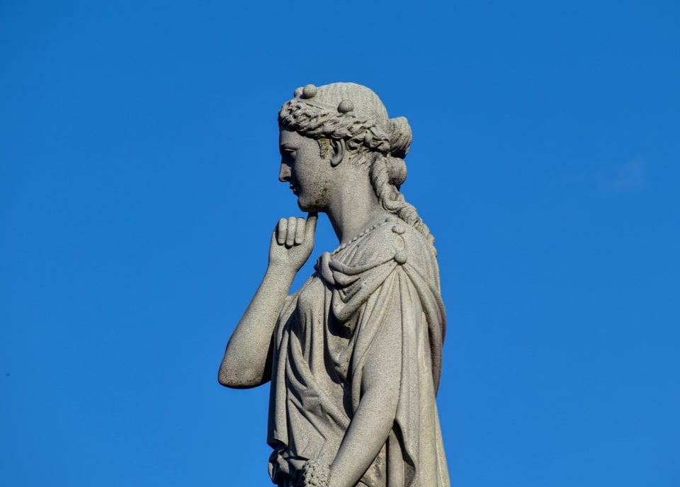 Statue of a woman with her hand on her chin with a sky blue backdrop
