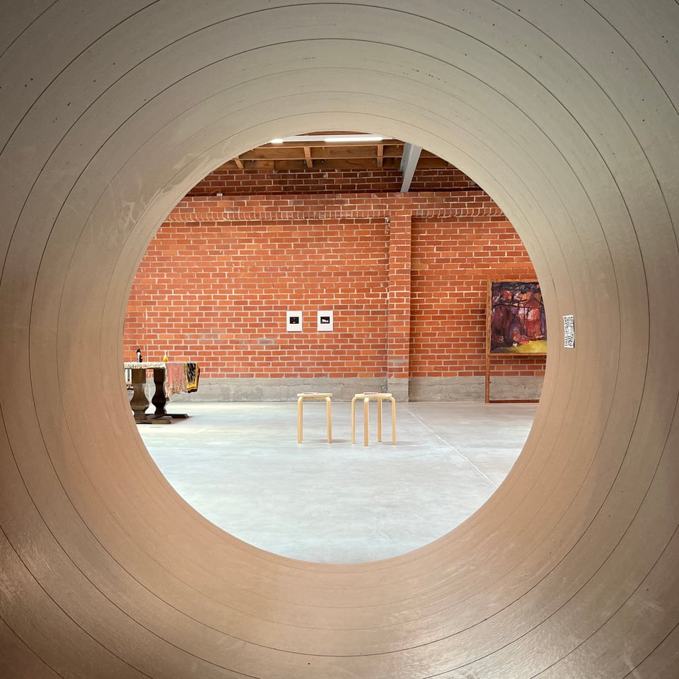 View of artworks against a brick wall seen from inside a large cardboard tube.
