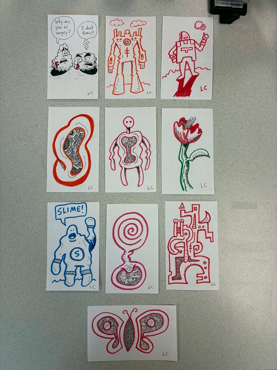 10 index cards on a desk--my desk, at work. Though it won't be much longer! On each index card there is a drawing. I drew them. There's a robot, a flower, a butterfly, lots of squiggles.