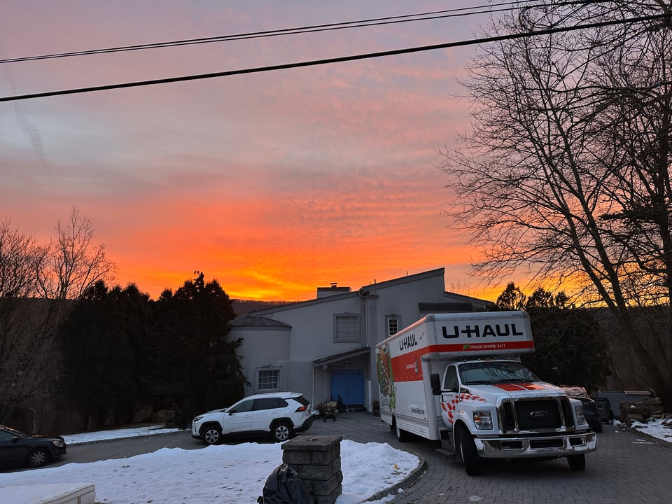 photo of a beautiful pink & gold sunrise behind a suburban home with a U-Haul truck in the driveway