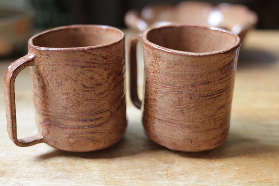 Two ceramic mugs side by side. They are nutmeg brown and have a tree bark texture.