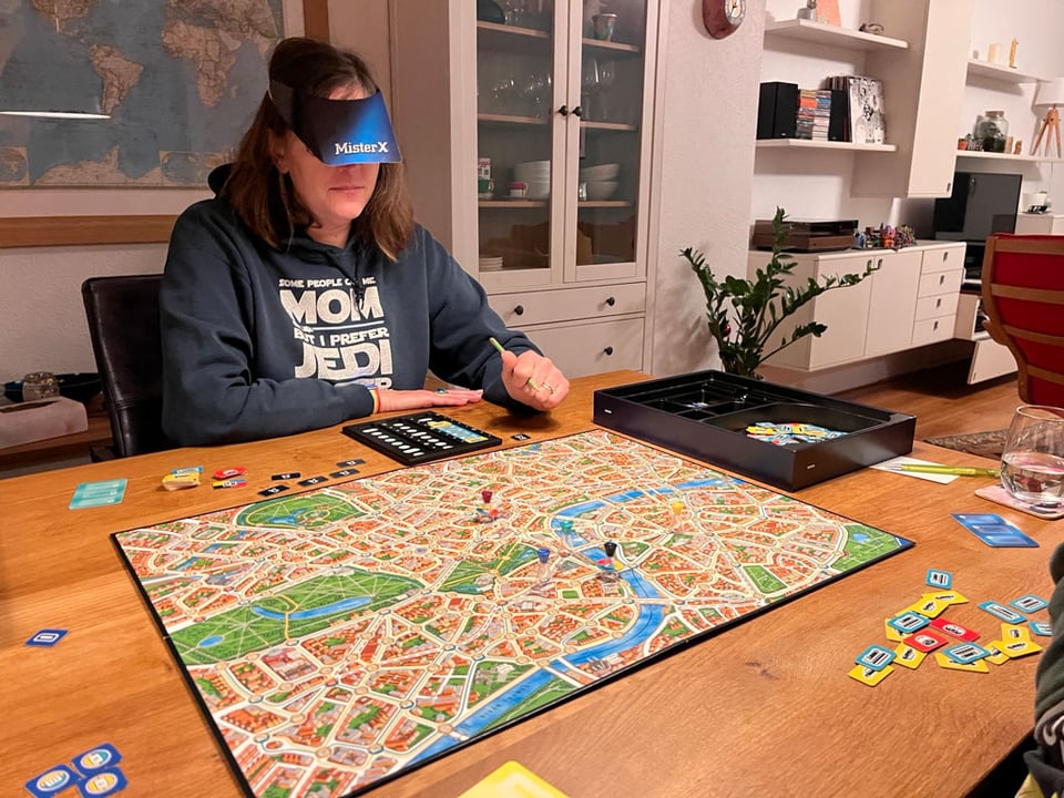 A woman plays a board game on a dining room table with her family off camera.