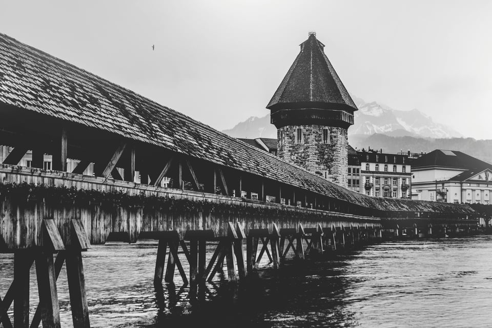 Black and white photo of a wooden bridge leading to an old European village