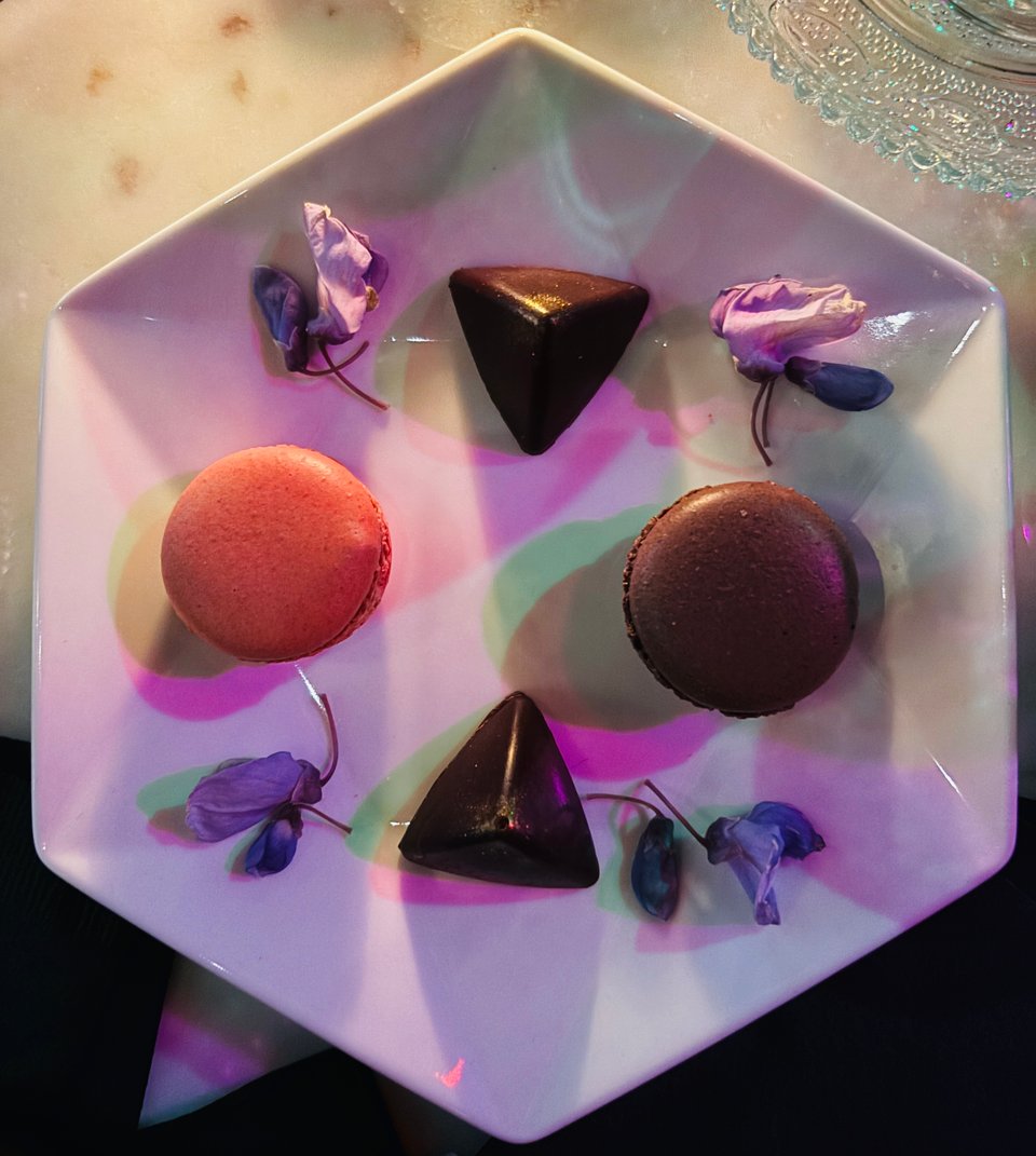 A light and dark macaron with 2 chocolate truffles arranged on octagonal plate with edible flowers.