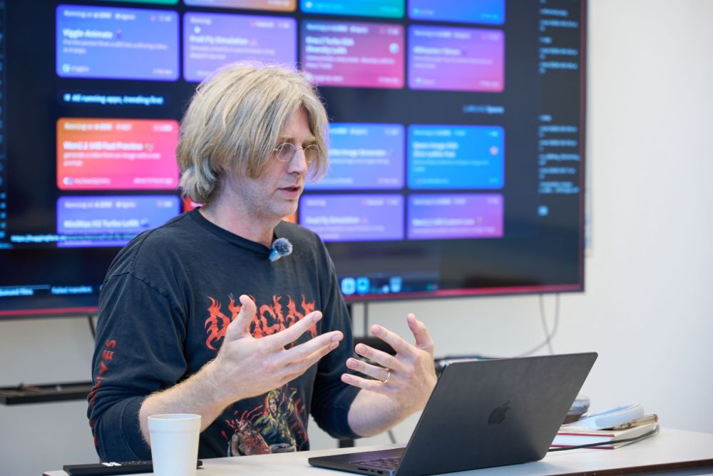 Geoffrey Lillemon speaking at the Netherlands Film Academy, gesturing with both hands in front of a laptop and a screen of colorful interface panels