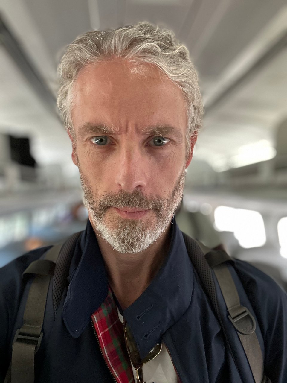 selfie of white man in navy Baracuta jacket, with backpack straps over his shoulders