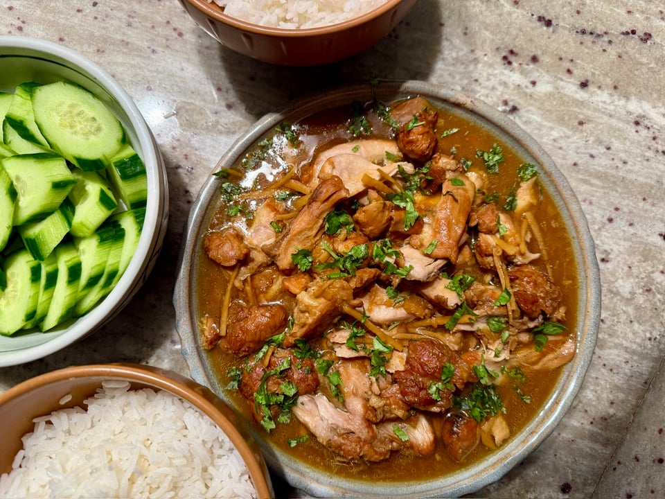 A big plate of shredded chicken in a caramel-colored sauce with raw cucumber and rice on the side.