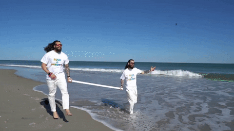 two men skipping on a beach carrying a pole