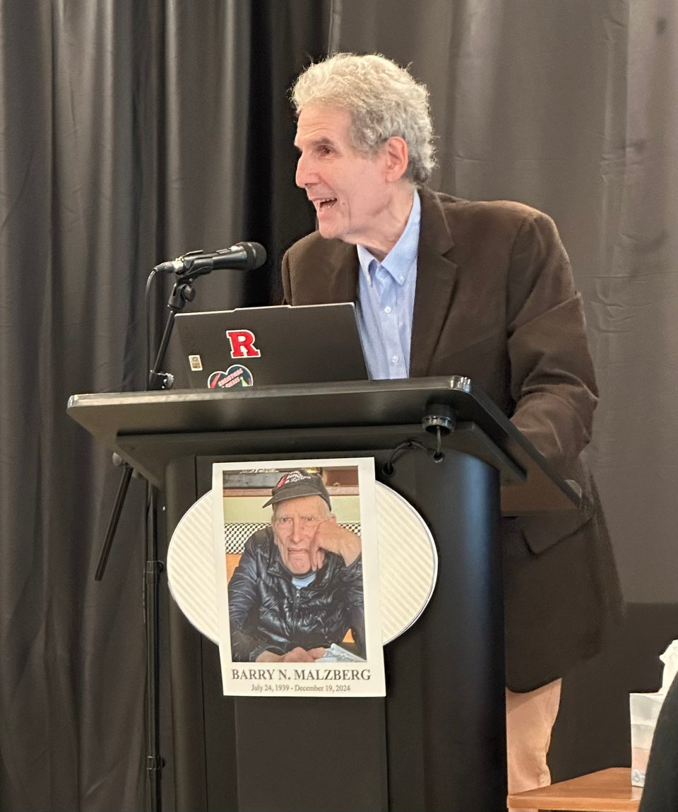 Photo of author Scott Edelman standing at a lectern that has a photo of author Barry N. Malzberg affixed to the front