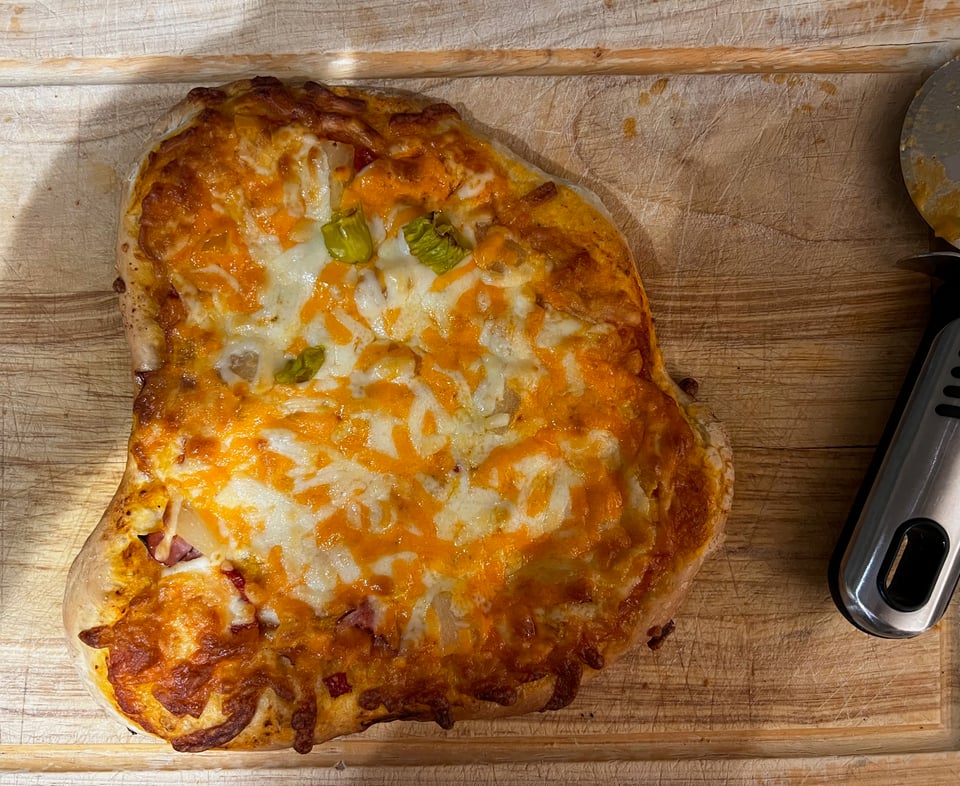 Photo of a homemade pizza as seen from above. A pizza cutter is visible on the side.