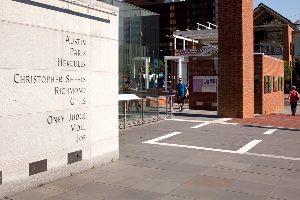A concrete wall with nine names carved on it: Austin, Paris, Hercules, Christopher Sheels, Richmond, Giles, Oney Judge, Moll, and Joe.