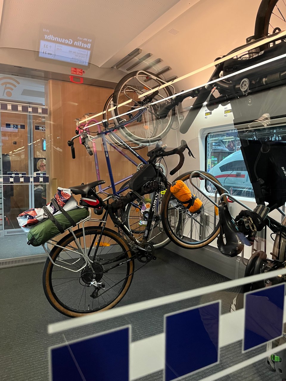 A bicycle with various luggage attachments hung up on a rack in a train compartment.