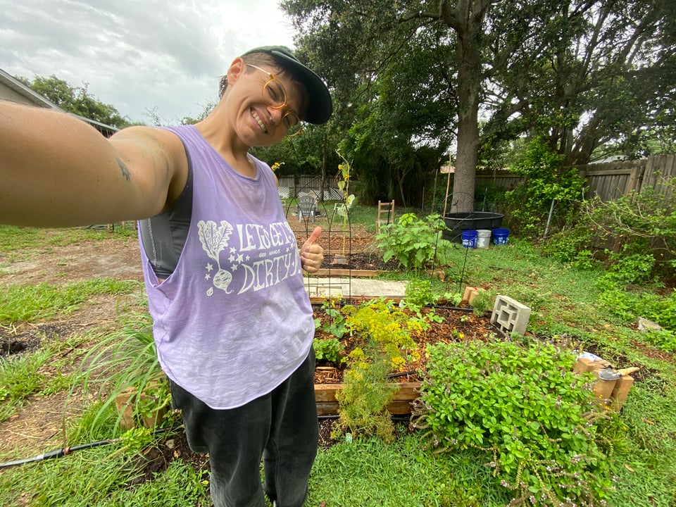 a photo of me in my garden, wearing a t-shirt i designed, that says “let’s get our hands dirty”