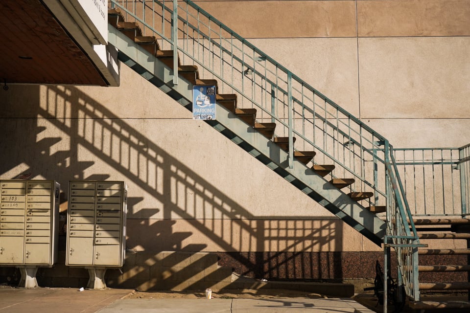 a set of metal stairs cast shadows on a wall in an LA strip mall