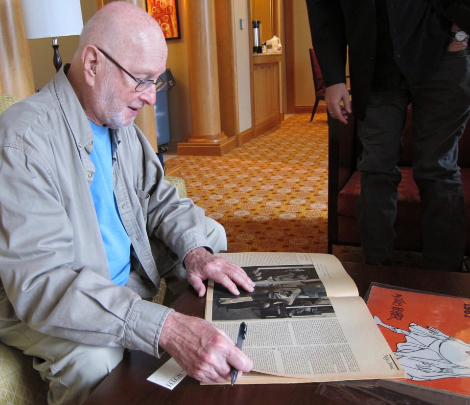 2014 photo of Jules Feiffer signing magazines and calendars