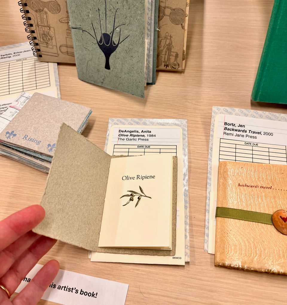 holding open a small handmade book with the illustration of an olive branch