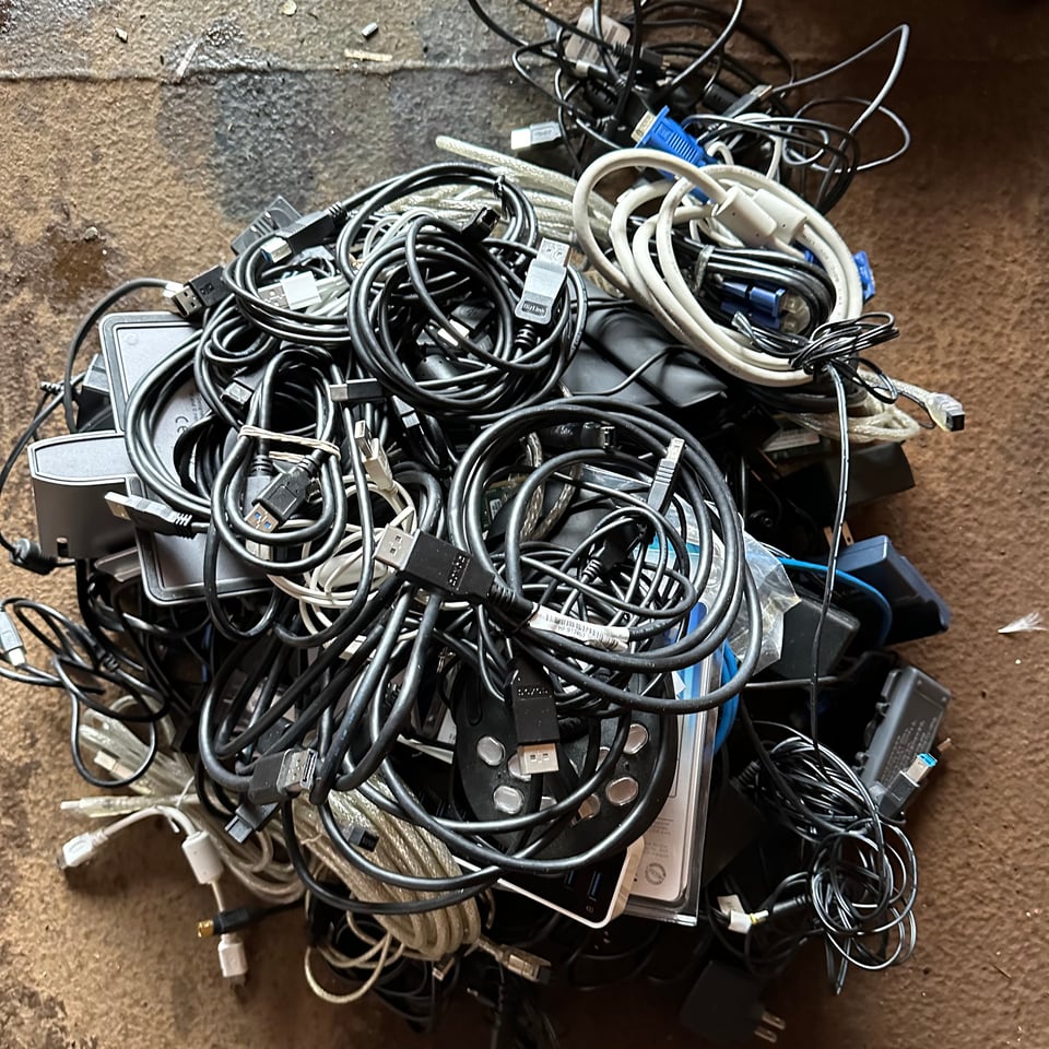 Photo of a pile of cables, connectors, and peripherals, on a rusty surface.