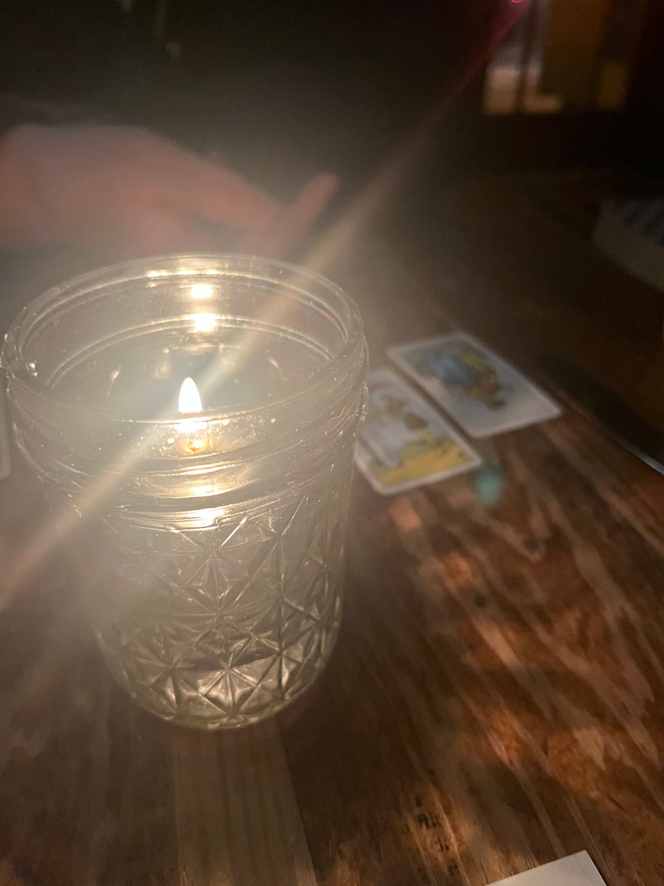 close-up of candle flame in glass mason jar, with tarot cards and a friend's hand in the background