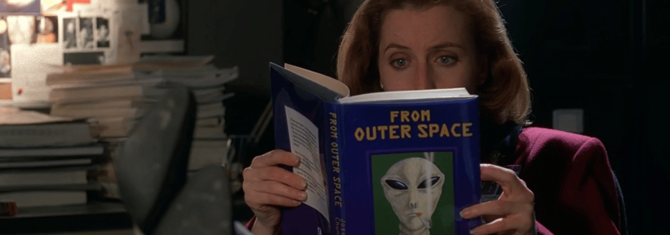 Dana Scully of the X-Files reads a book titled "From Outer Space." It features an alien smoking a cigarette on the cover.