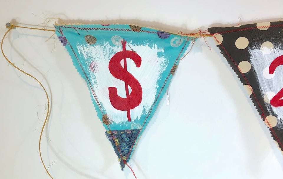 A triangle flag banner sewn with red thread on twine string that reads $ sign