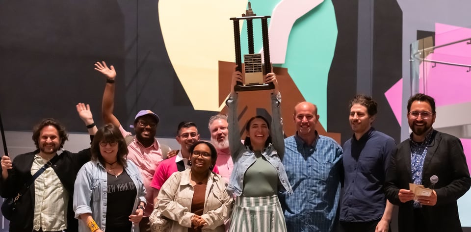 A team of 9 holds a trophy containing buildings from the New York Panorama